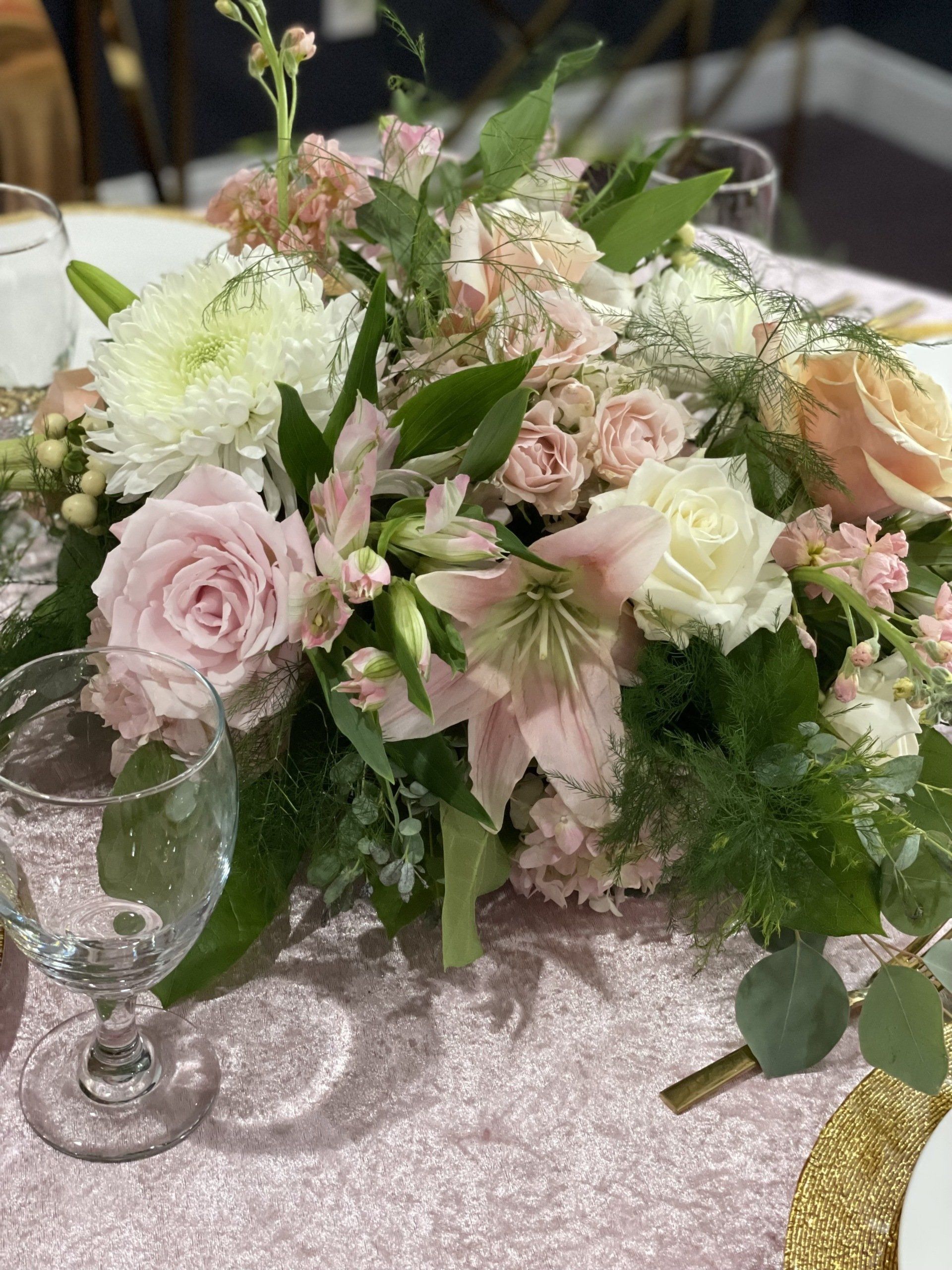 Soft pink and white floral centerpiece with greenery arranged on a dining table