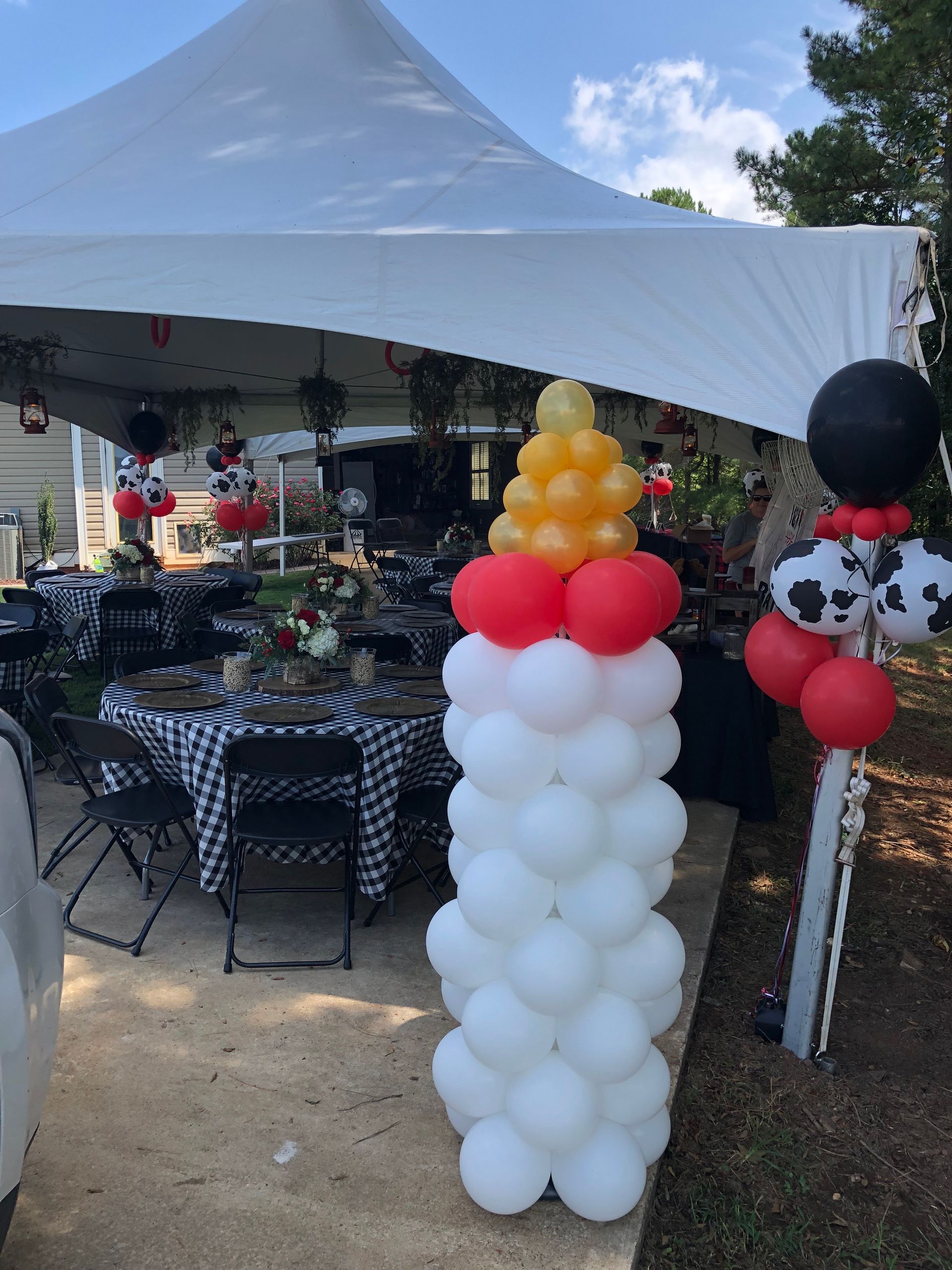 Balloon columns set under a large white outdoor event tent for a celebration