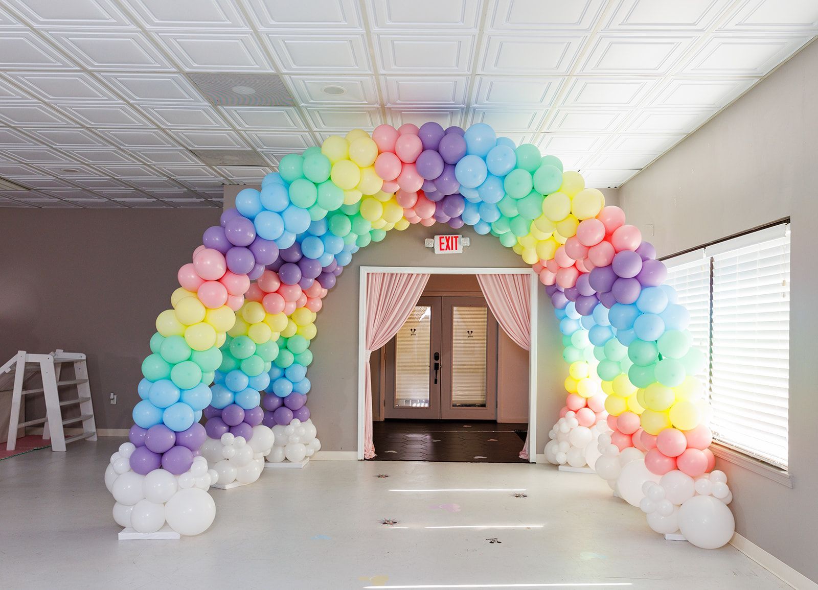 Rainbow balloon arch framing a doorway inside an event space