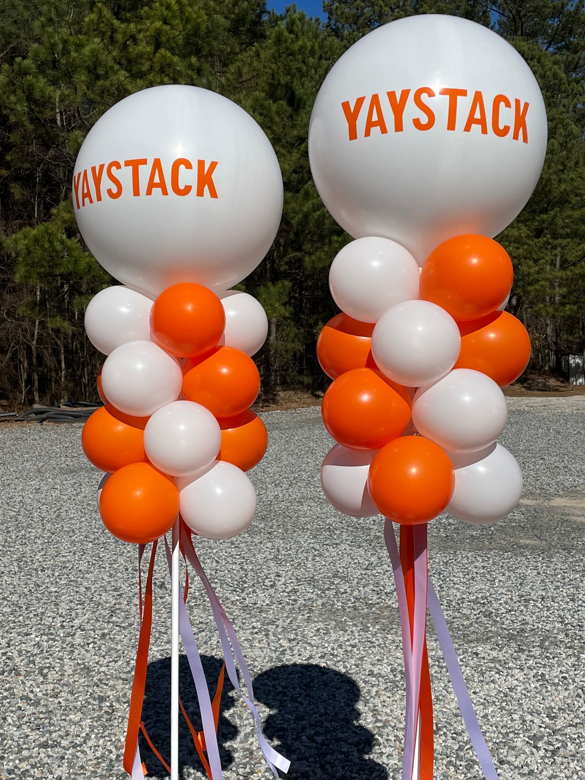 Branded white balloon toppers with orange and white balloon bases set outdoors for an event