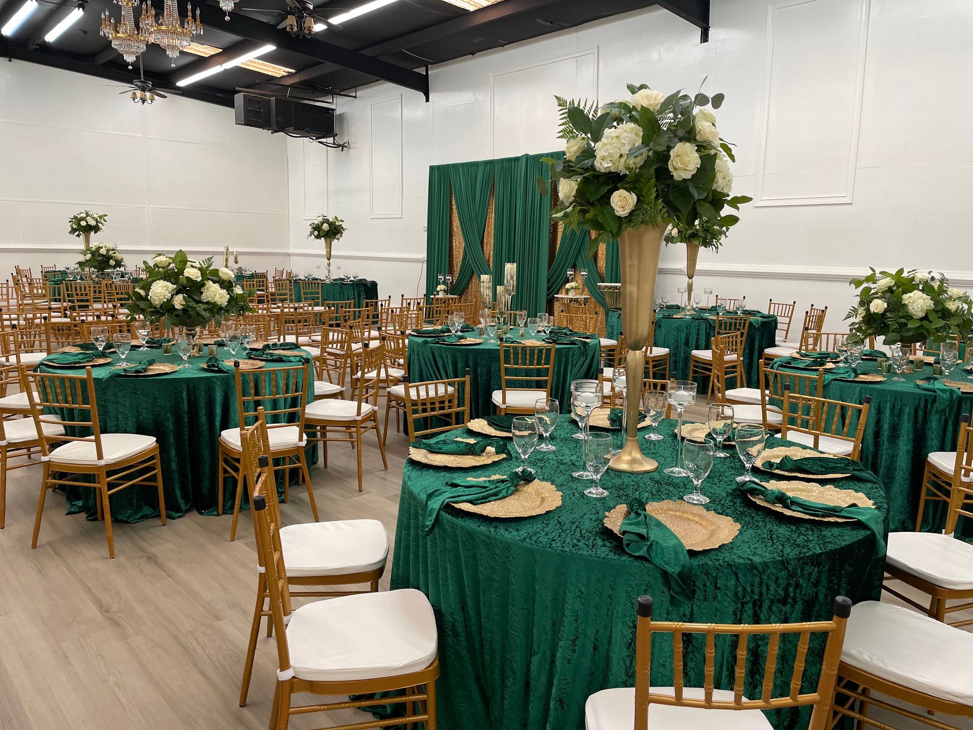 Elegant reception setup with green linens, gold chairs, and tall floral centerpieces