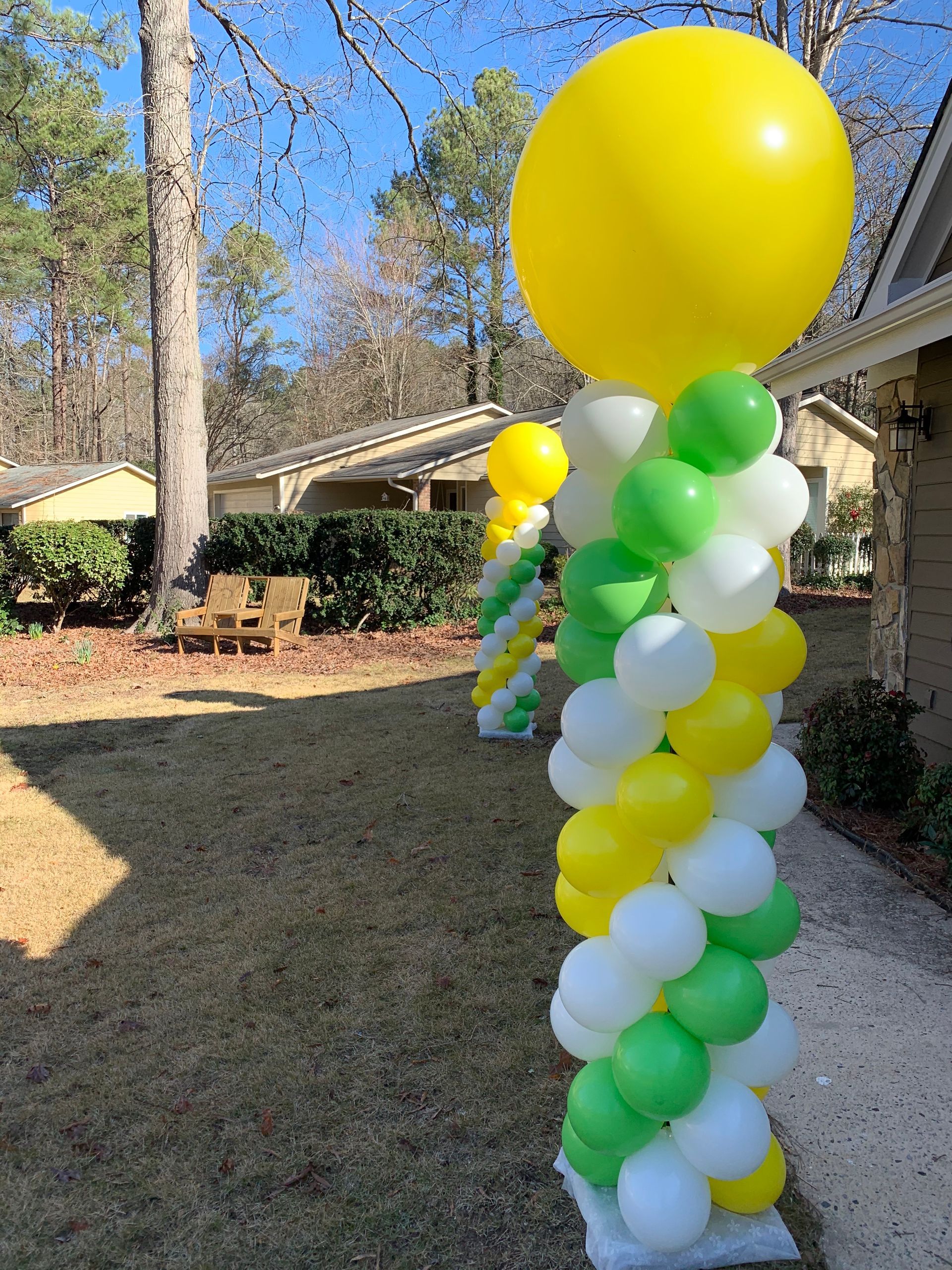 Yellow, green, and white balloon column displayed outdoors along a walkway
