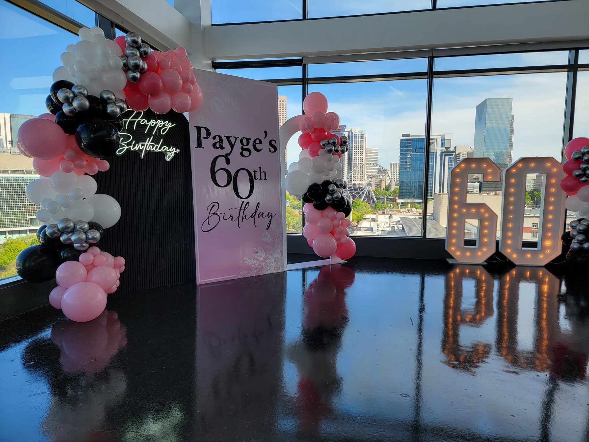 Pink black and white balloon décor with marquee numbers and custom 60th birthday backdrop at city view venue