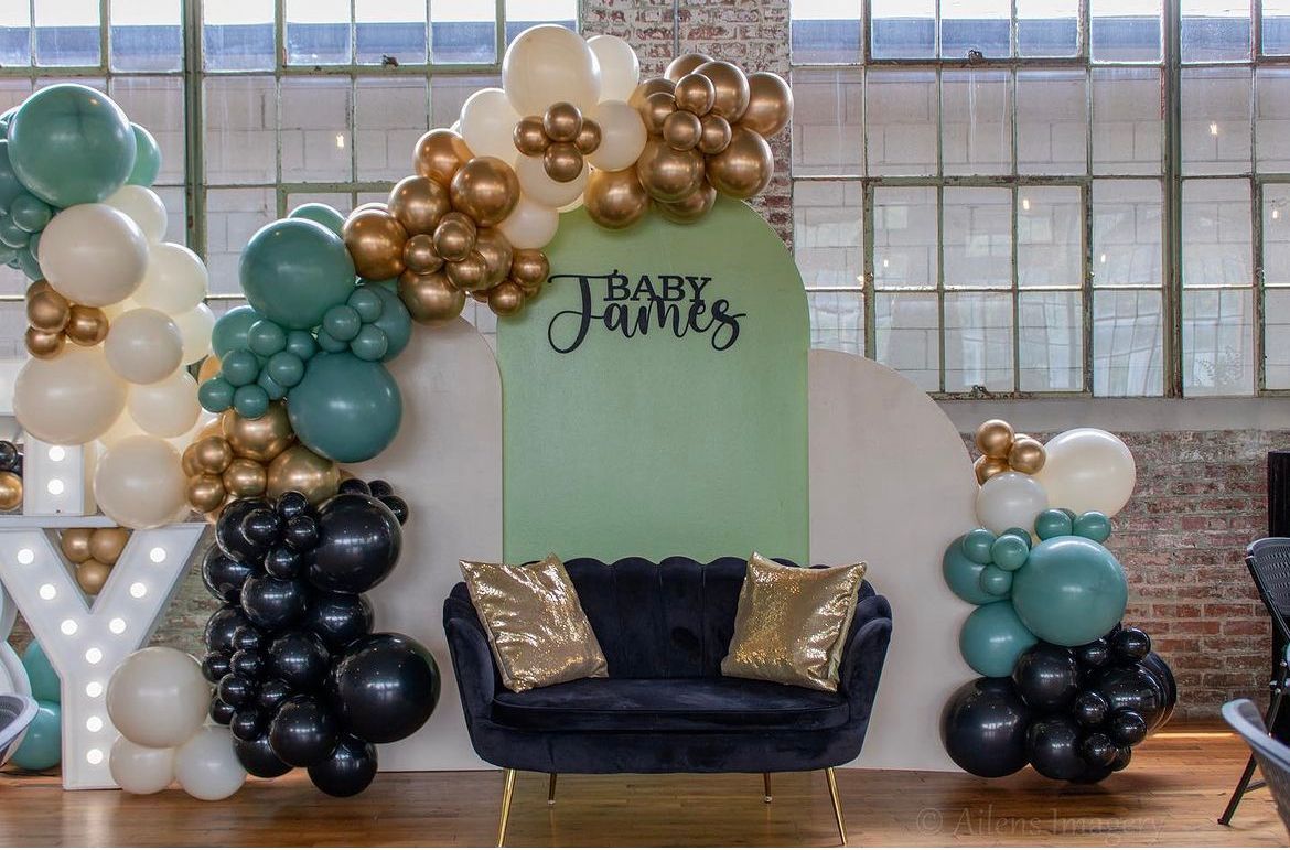 Green gold black and white balloon arch with baby shower backdrop and lounge seating
