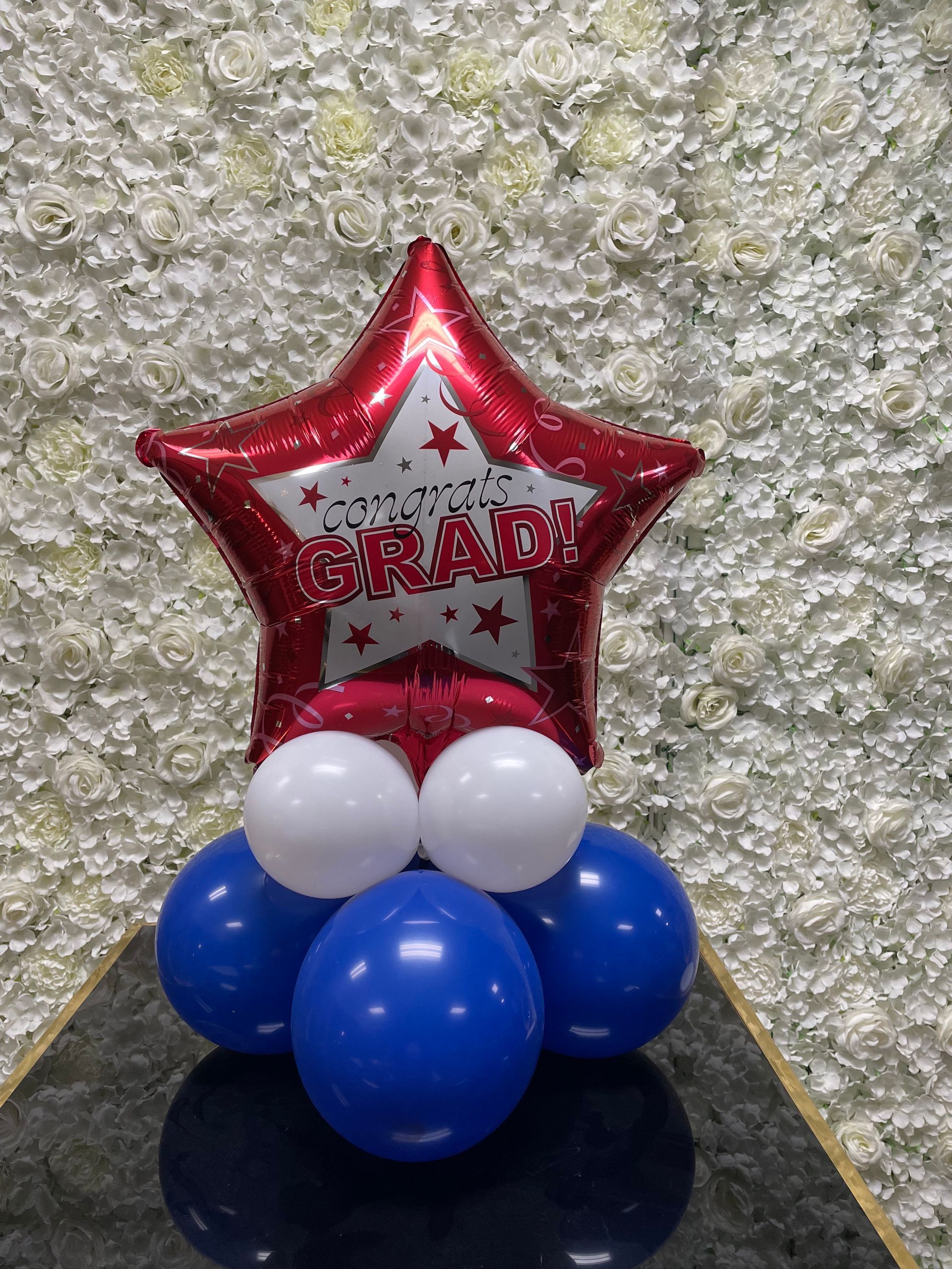 Red star-shaped congrats grad foil balloon against a white floral backdrop