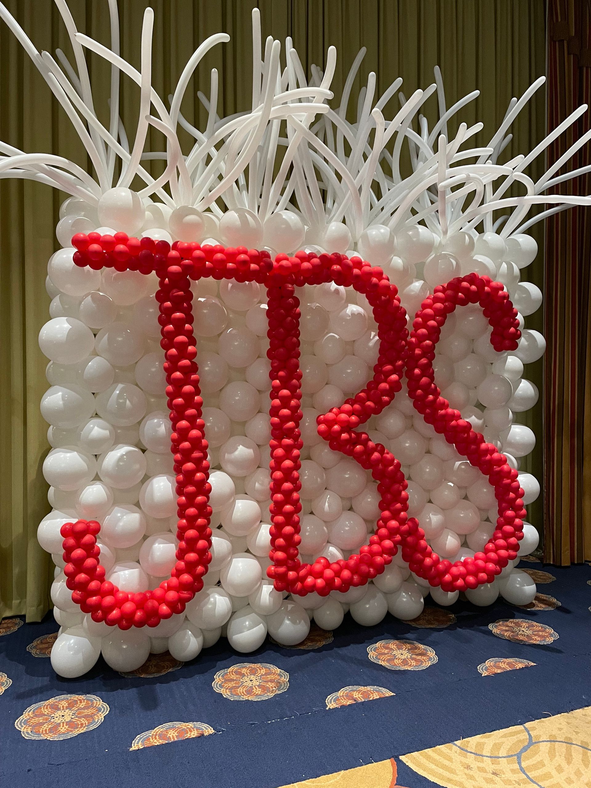 White balloon sculpture centerpiece with red balloon lettering and tall twisting accents for themed event décor