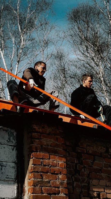 Two people standing on a rooftop behind an orange safety rail, looking outward under a blue sky.