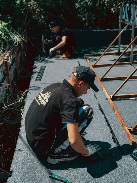 Two workers installing roofing material on a flat roof, one kneeling in the foreground.