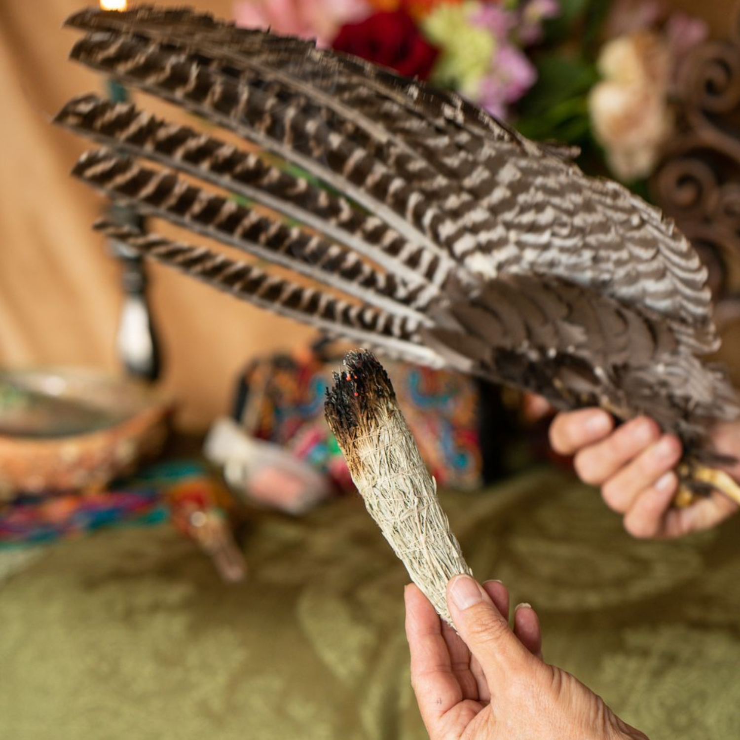 Hands holding a black-and-white feather and a small feathered piece over a green cloth table at Enlightened Life Temple