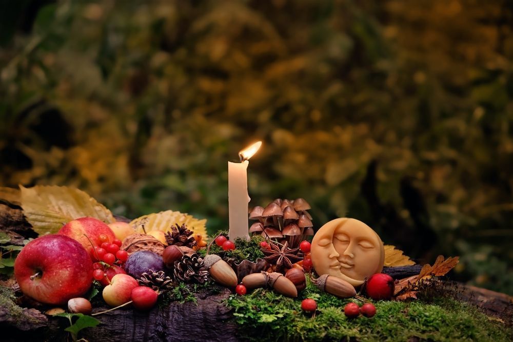 Autumn harvest still life with fruit, nuts, a lit candle, and a carved face on mossy ground at Enlightened Life Temple