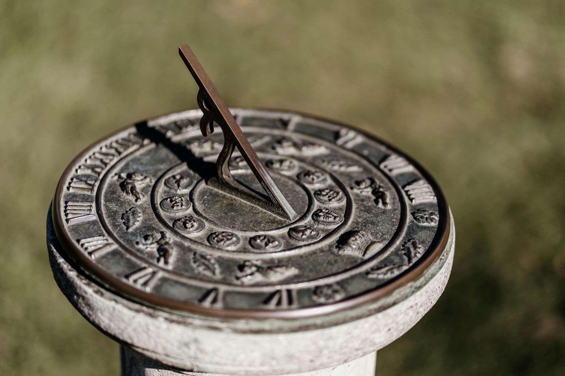 Metal sundial on a stone pedestal, with a brown gnomon casting a shadow outdoors at Enlightened Life Temple