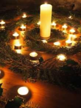 Candlelit evergreen wreath with a tall central candle and small glowing tealights on a wooden table at Enlightened Life Temple