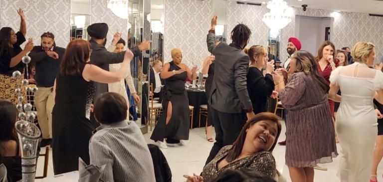 Guests dancing at a formal indoor celebration with chandeliers and elegant decor.