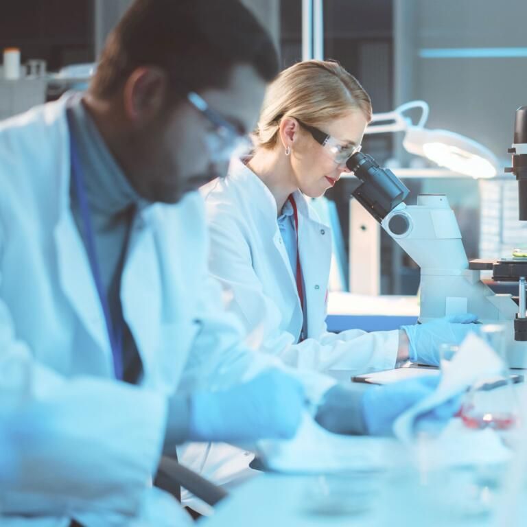 Scientists in lab coats using microscopes in a bright laboratory