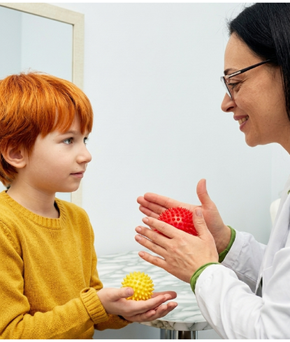 Therapist and child facing each other, holding colorful textured balls in a bright room.