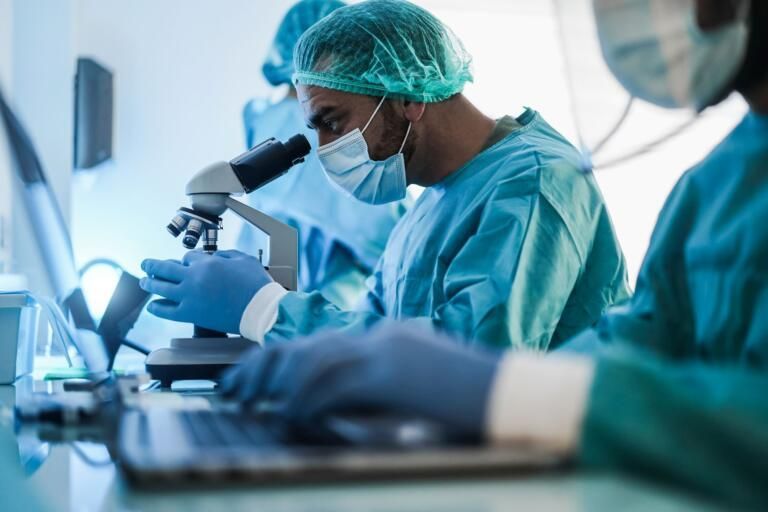 Scientists in blue scrubs working at microscopes in a laboratory
