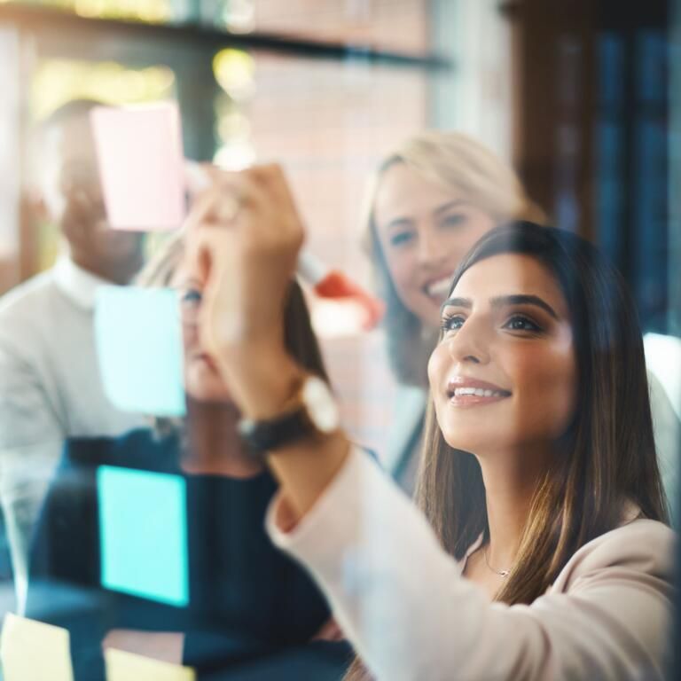 Colleagues in a meeting room placing colorful sticky notes on a glass wall