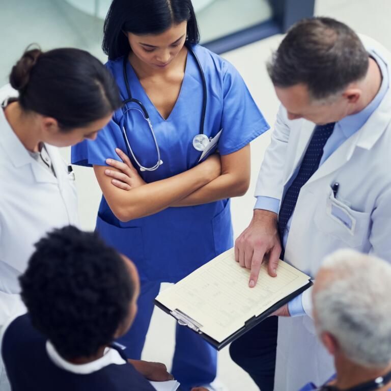 Medical team in blue and white scrubs reviewing notes with patients in a clinical setting