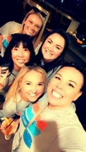 Five smiling friends posing close together for a selfie at night, one wearing a blue diamond-patterned shirt
