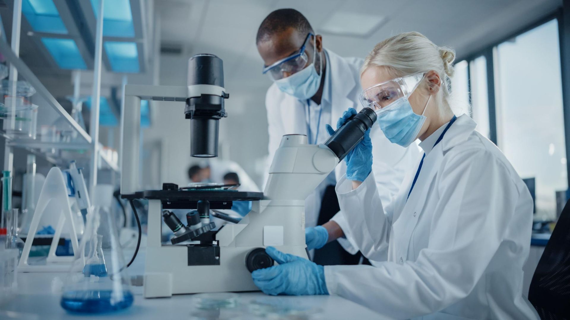 Two scientists in lab coats examining a sample under a microscope in a modern laboratory
