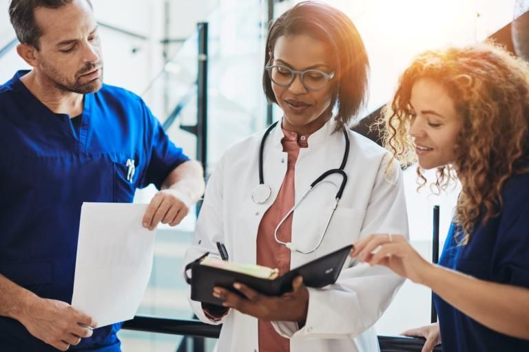 Three medical professionals discussing a tablet and documents in a bright clinic hallway