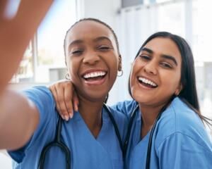 Two smiling healthcare workers in blue scrubs posing together indoors