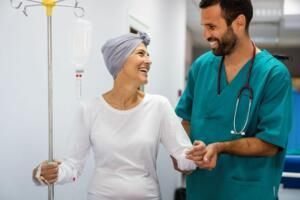 Patient in white shirt smiling with a nurse in teal scrubs beside an IV pole in a hospital room