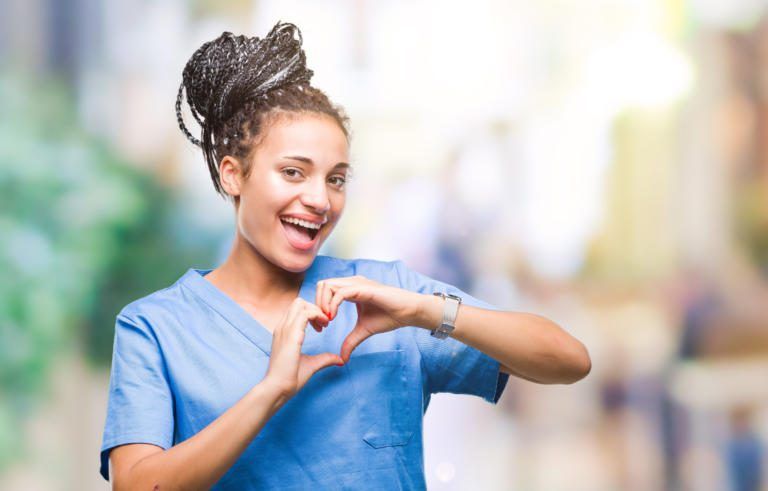 Smiling healthcare worker in blue scrubs making a heart shape with her hands