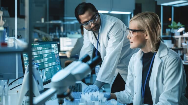 Two scientists in lab coats reviewing data at a computer in a modern laboratory