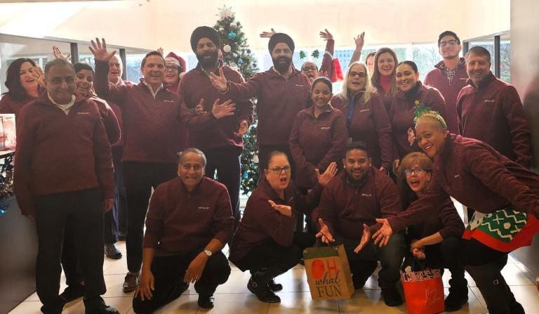 Group of people in maroon uniforms posing indoors, smiling and waving at the camera.