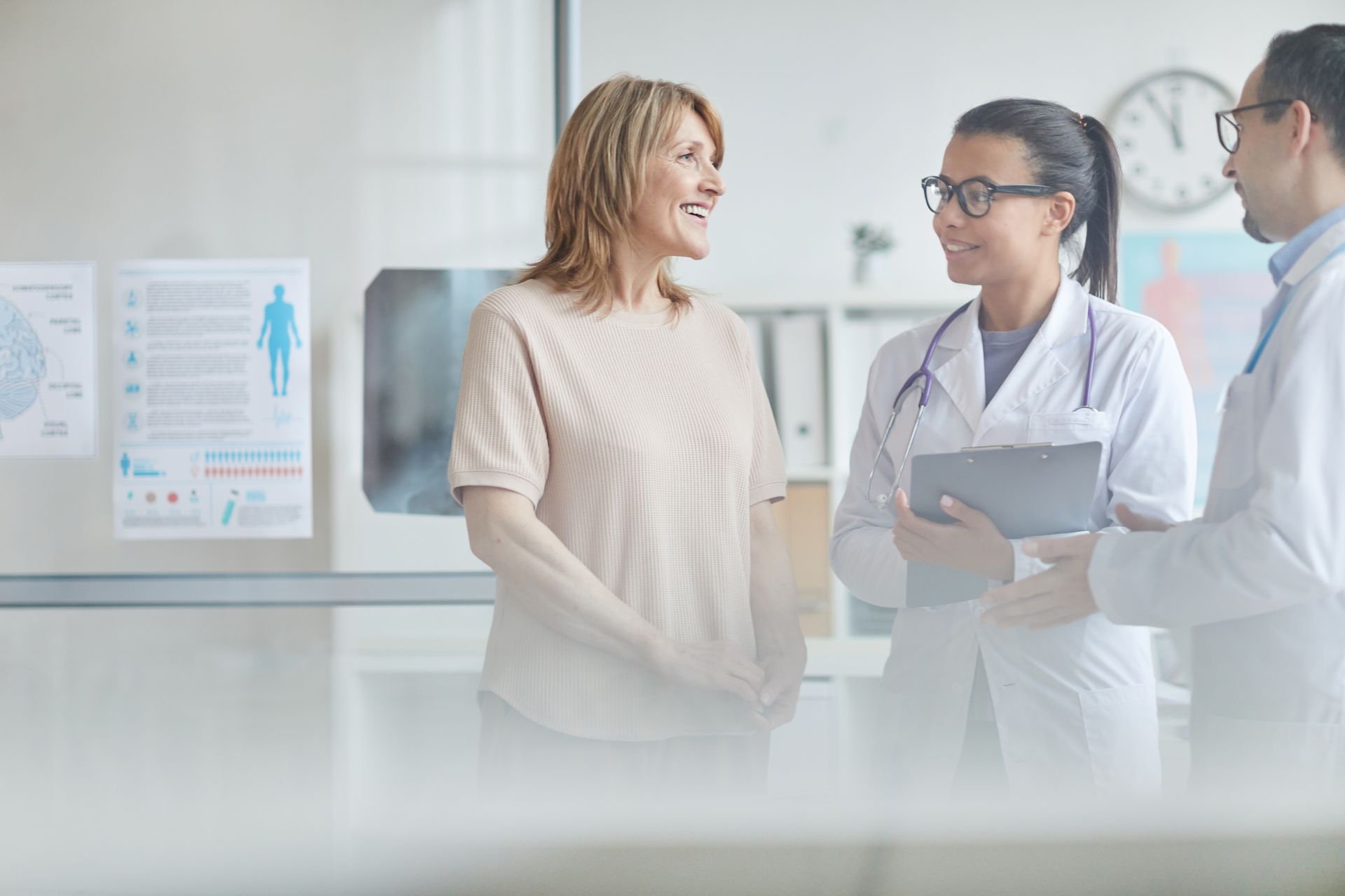 Doctor speaking with a smiling patient in a bright clinic, with another clinician nearby.