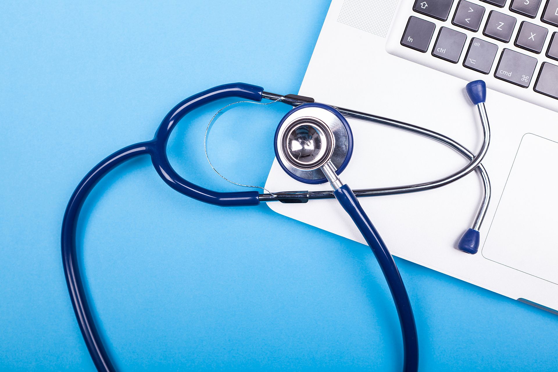 Blue stethoscope on a laptop keyboard against a light blue background