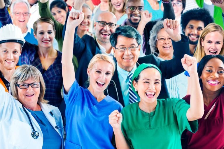 Smiling healthcare workers in colorful scrubs cheering with raised fists in a bright group photo