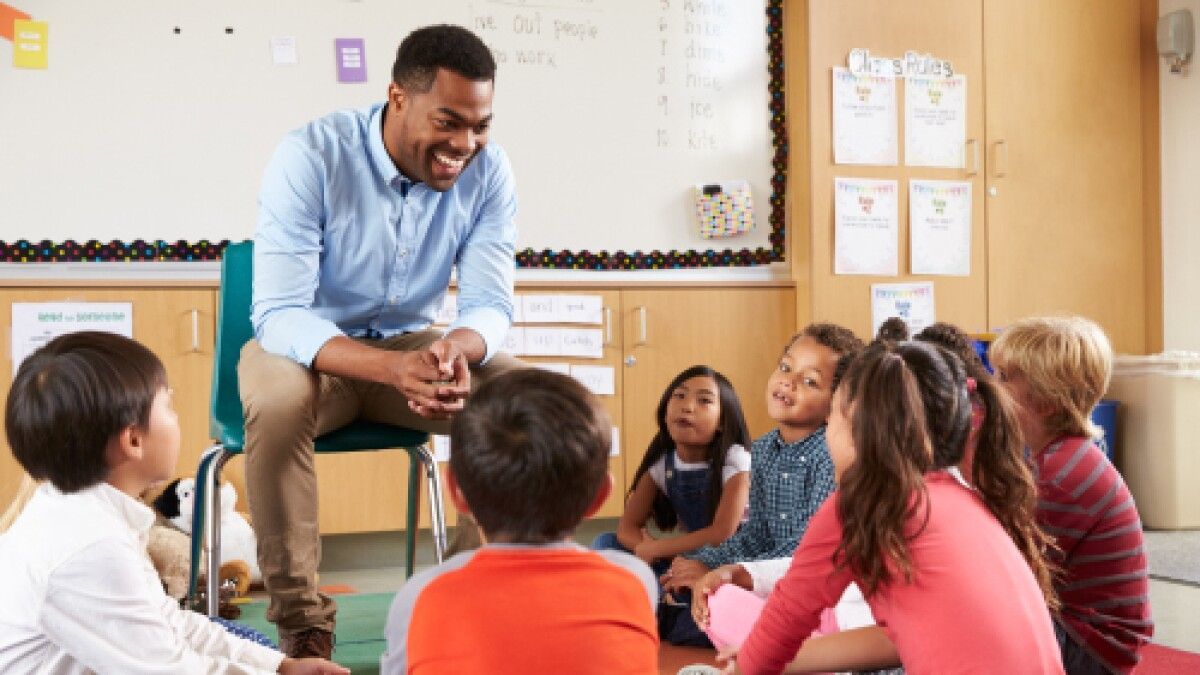 Teacher leaning toward a group of children seated on the floor in a classroom, engaging them in discussion