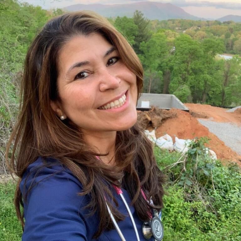 Smiling woman taking a selfie on a scenic hillside with green trees and mountains in the background