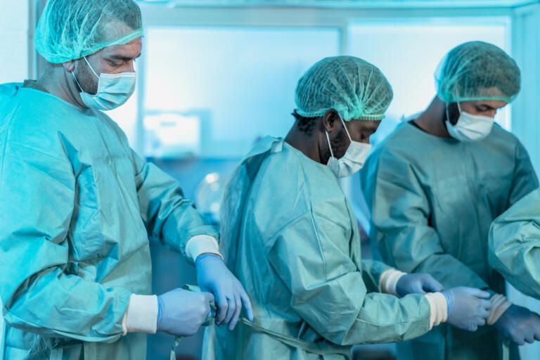 Healthcare workers in blue surgical gowns and masks preparing for an operation in a sterile room