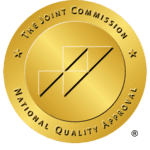 The Joint Commission National Quality Approval gold seal with black diagonal lines and text around the edge