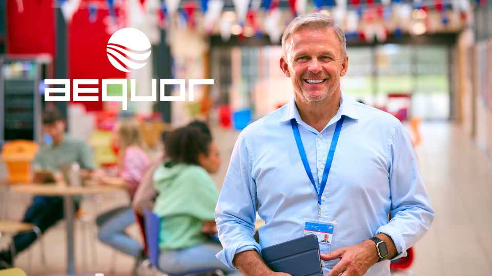Smiling man in a blue shirt holding a folder at a trade show booth with blurred attendees and flags in background