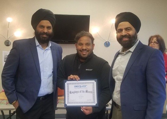 Three people in suits smiling, holding a framed certificate indoors.