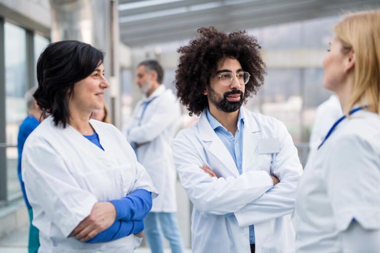 Doctors in white coats talking in a hospital hallway, arms crossed
