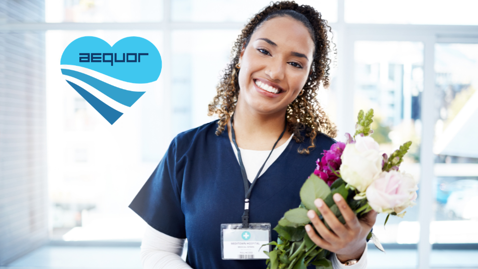 Smiling employee in navy scrubs holding flowers in a bright office lobby with a company logo