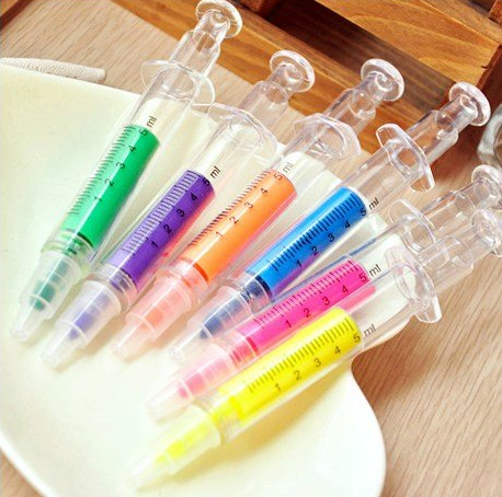 Colorful syringe-shaped pens with green, purple, orange, blue, pink, and yellow ink on a wooden tray