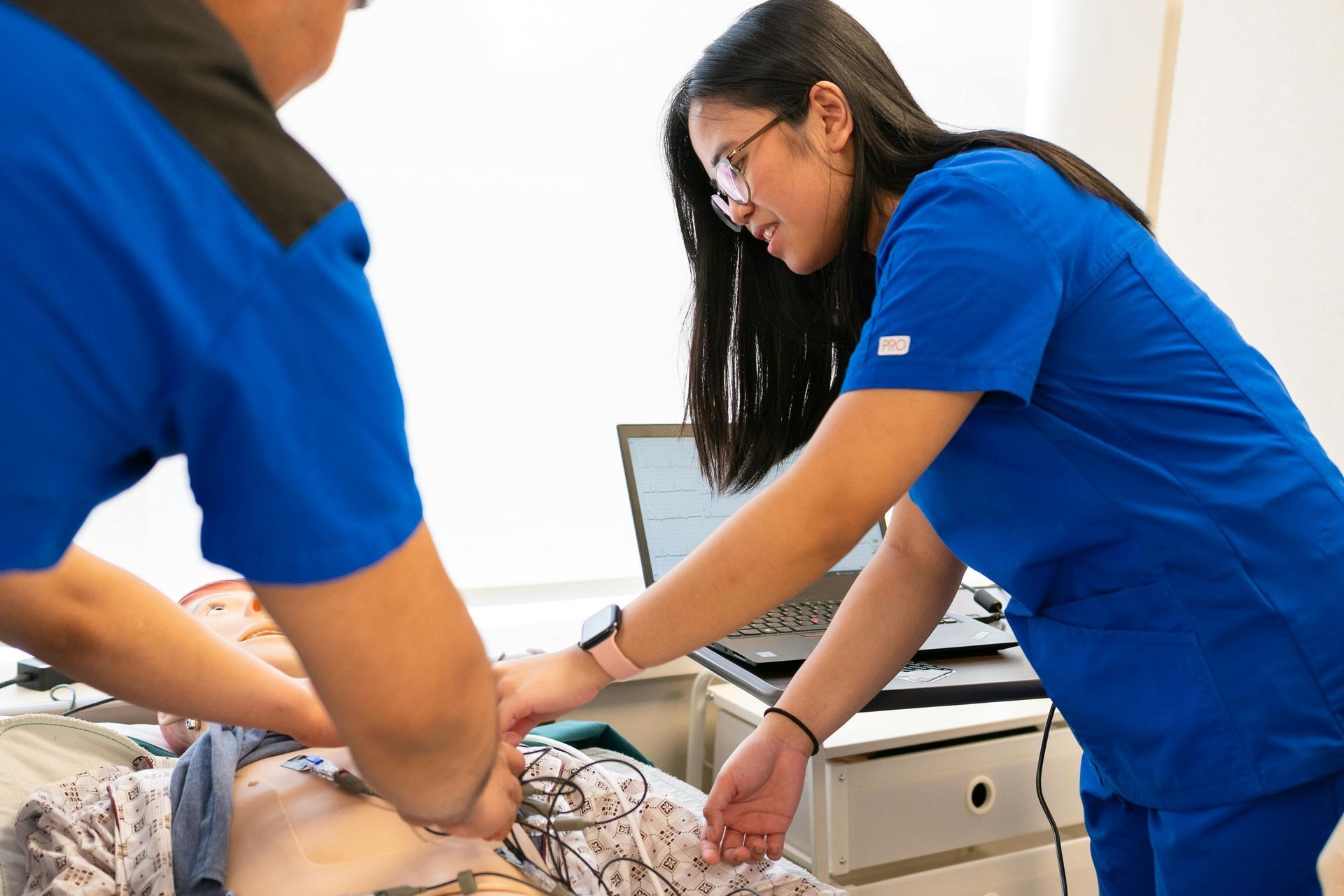 Two healthcare workers in blue scrubs adjusting a patient on a hospital bed