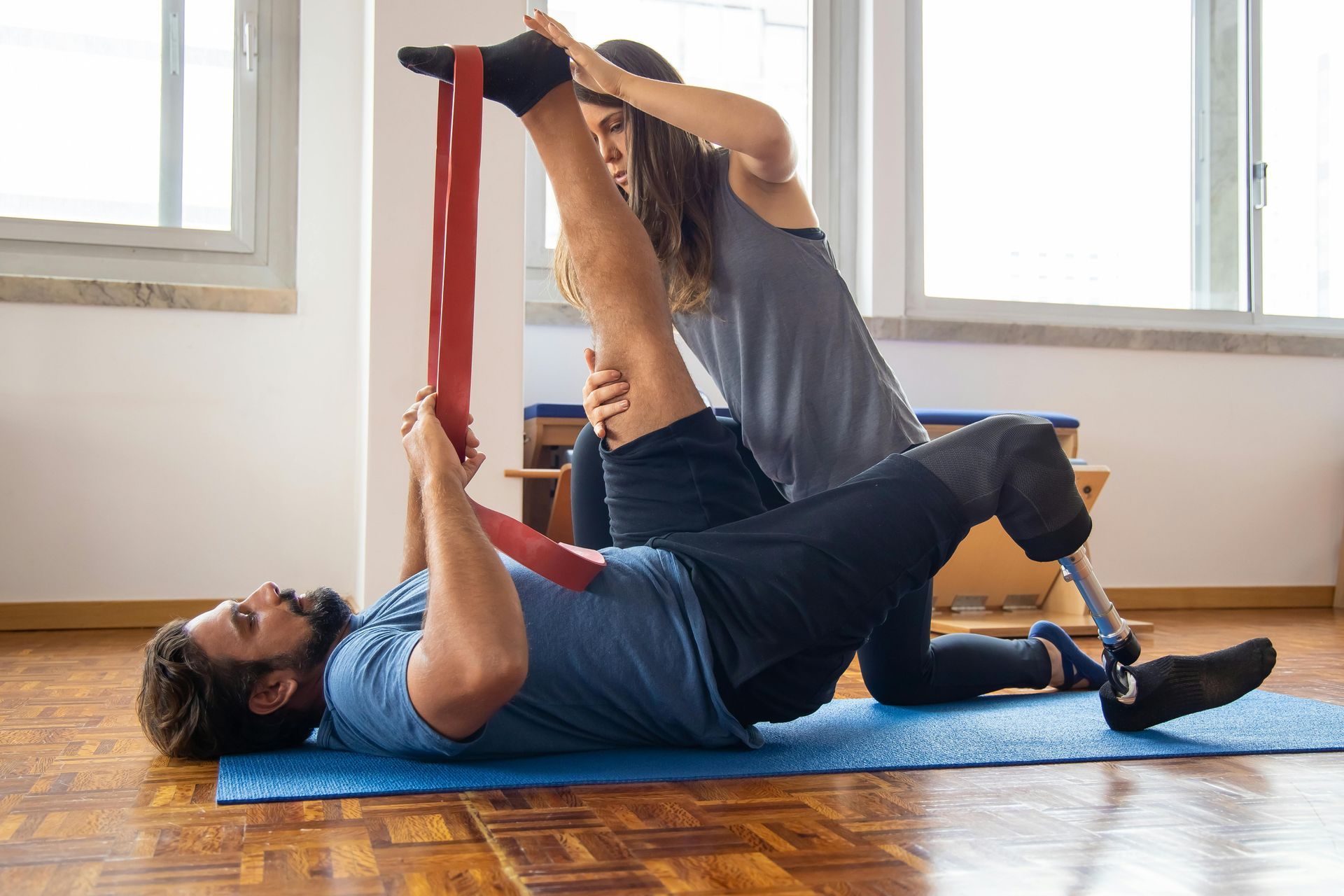 Two people doing assisted stretching with a red strap in a bright studio