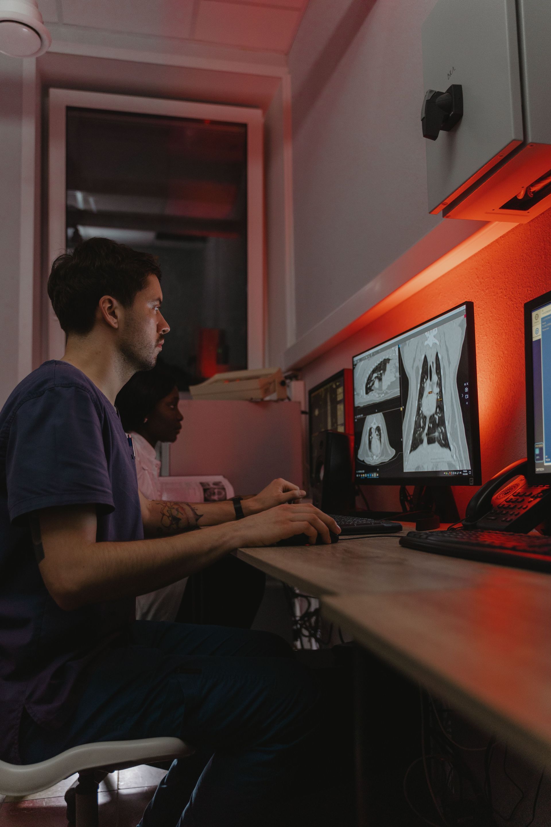 Person reviewing X-ray scans on dual monitors in a dimly lit workspace with orange lighting