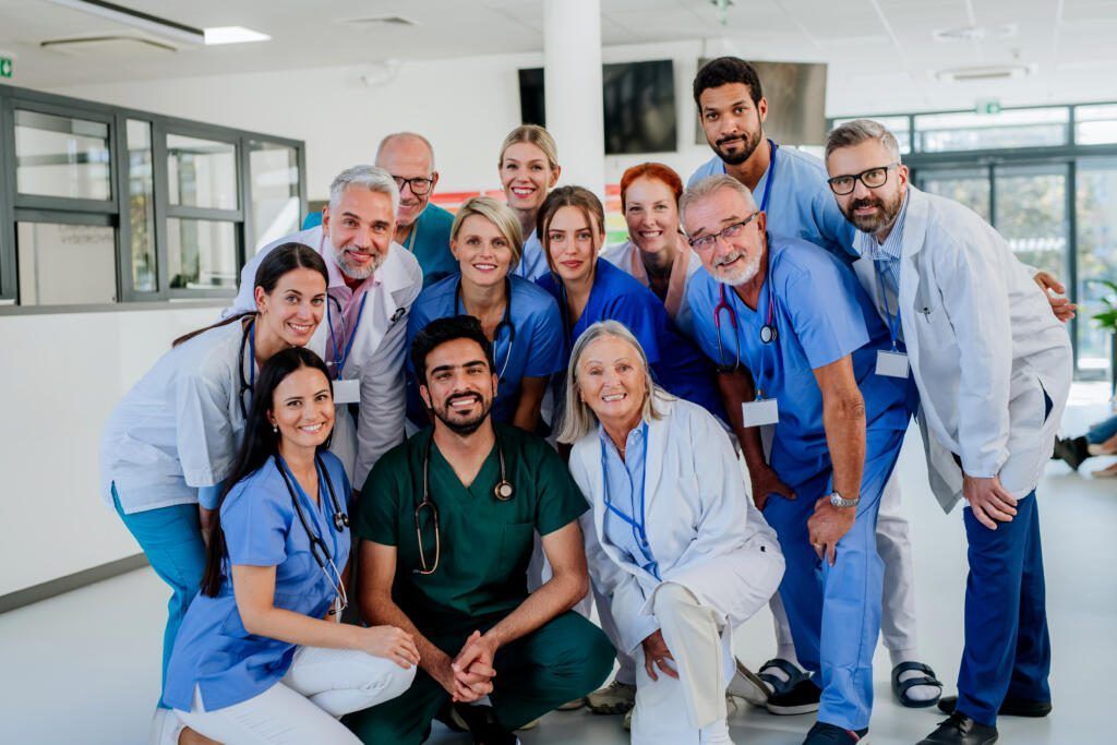 Group of medical staff in blue and white uniforms posing together in a bright hospital hallway