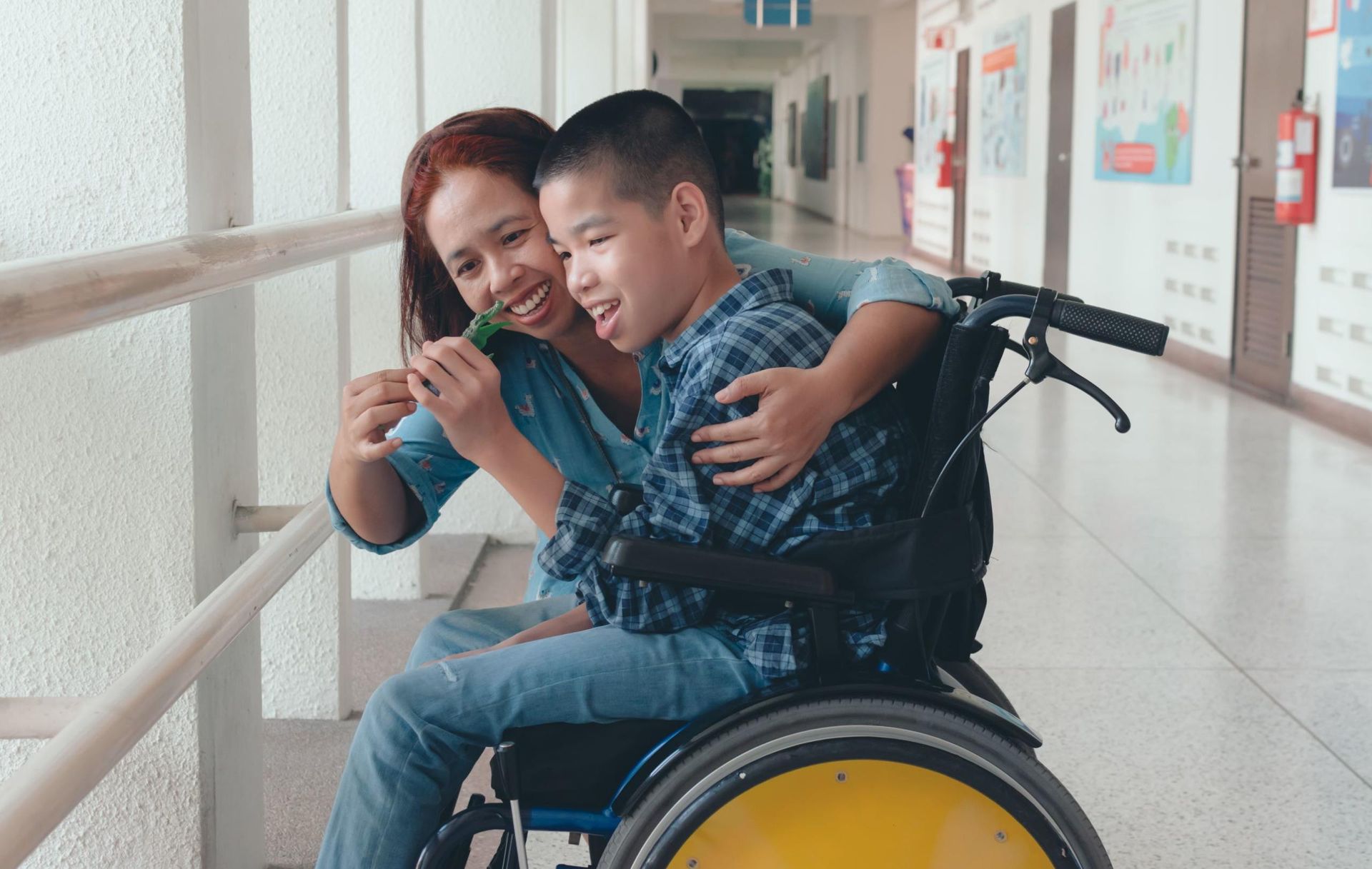 Two people smiling in a wheelchair by a bright hallway window