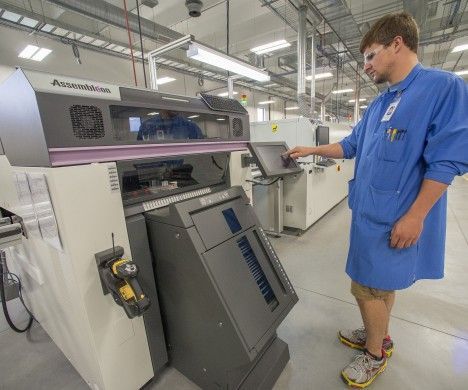 Man in blue lab coat operating industrial machine in a factory.