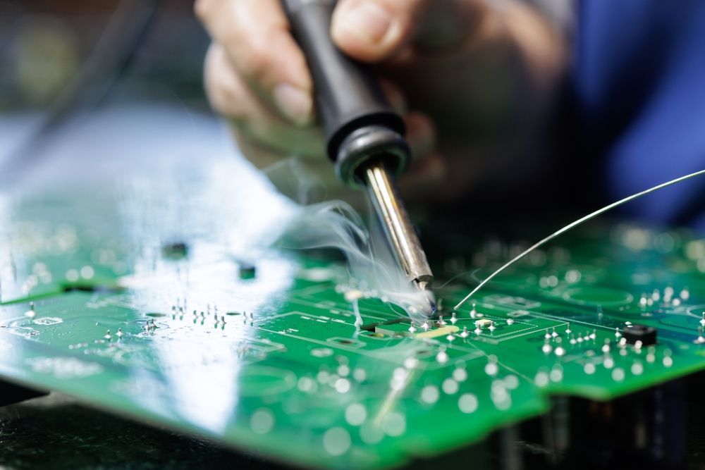 Soldering iron repairing a green circuit board with smoke rising