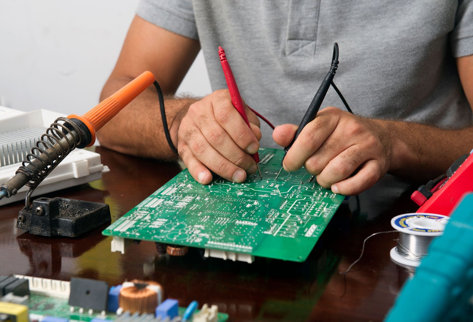 Person soldering a green circuit board on a workbench with tools nearby